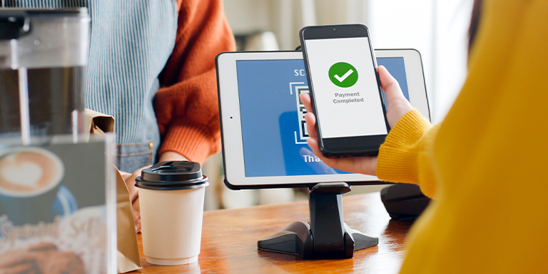 Photo of customer scanning a QR code with their phone to make a purchase in a cafe.